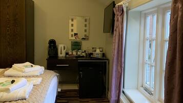 A hotel room with a bed, a small kitchenette, a mirror, and a window with curtains.