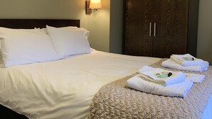 A neatly made bed with white linens and a beige quilted throw, a wooden wardrobe with two doors, and a wall-mounted lamp. - George & Dragon (Chester)