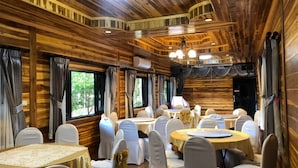 A wooden interior with round tables and white chairs, large windows, and a chandelier. - Hugpua Hotel (Pua)