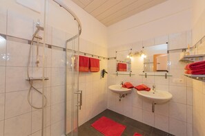 A bathroom with a glass shower enclosure, two sinks, and multiple red towels. - Landhaus Hochkönig (Muehlbach Am Hochkoenig)