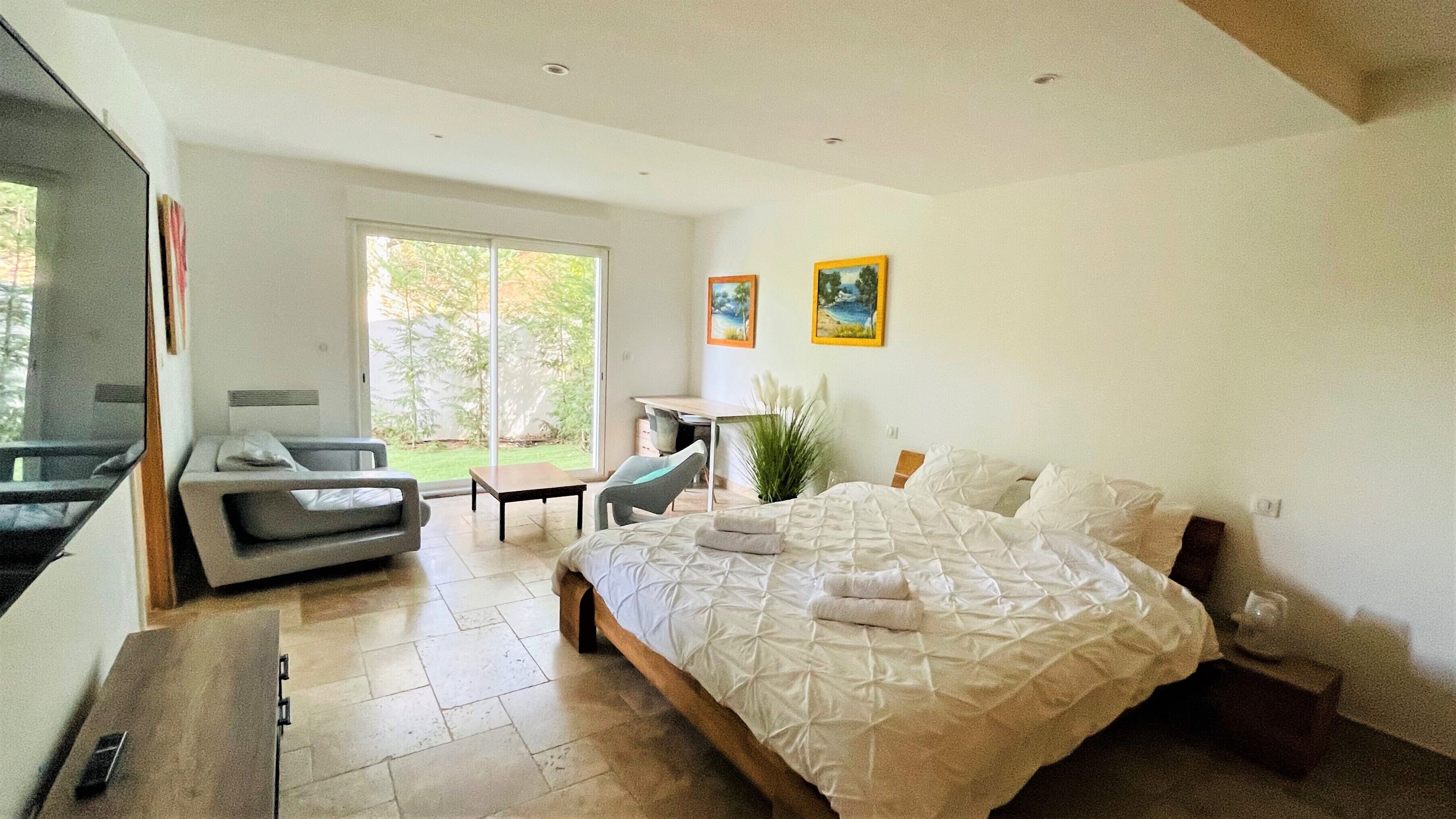 A modern bedroom with a large bed, a sofa, a desk, and a view of the outdoors.