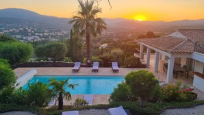 A pool with lounge chairs, surrounded by greenery and a view of a town and mountains in the background.