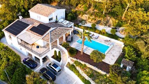 A modern house with a swimming pool, solar panels, and a garage with multiple cars.