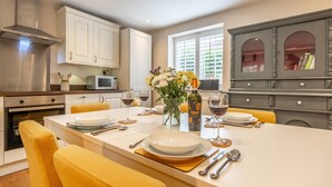 A modern kitchen with white cabinets, a central island with yellow chairs, and a dining table set for six. - Sherbet Cottage, South Creake, Norfolk (Fakenham)