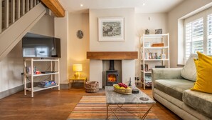A living room with a fireplace, a television, a sofa, and a bookshelf. - Sherbet Cottage, South Creake, Norfolk (Fakenham)