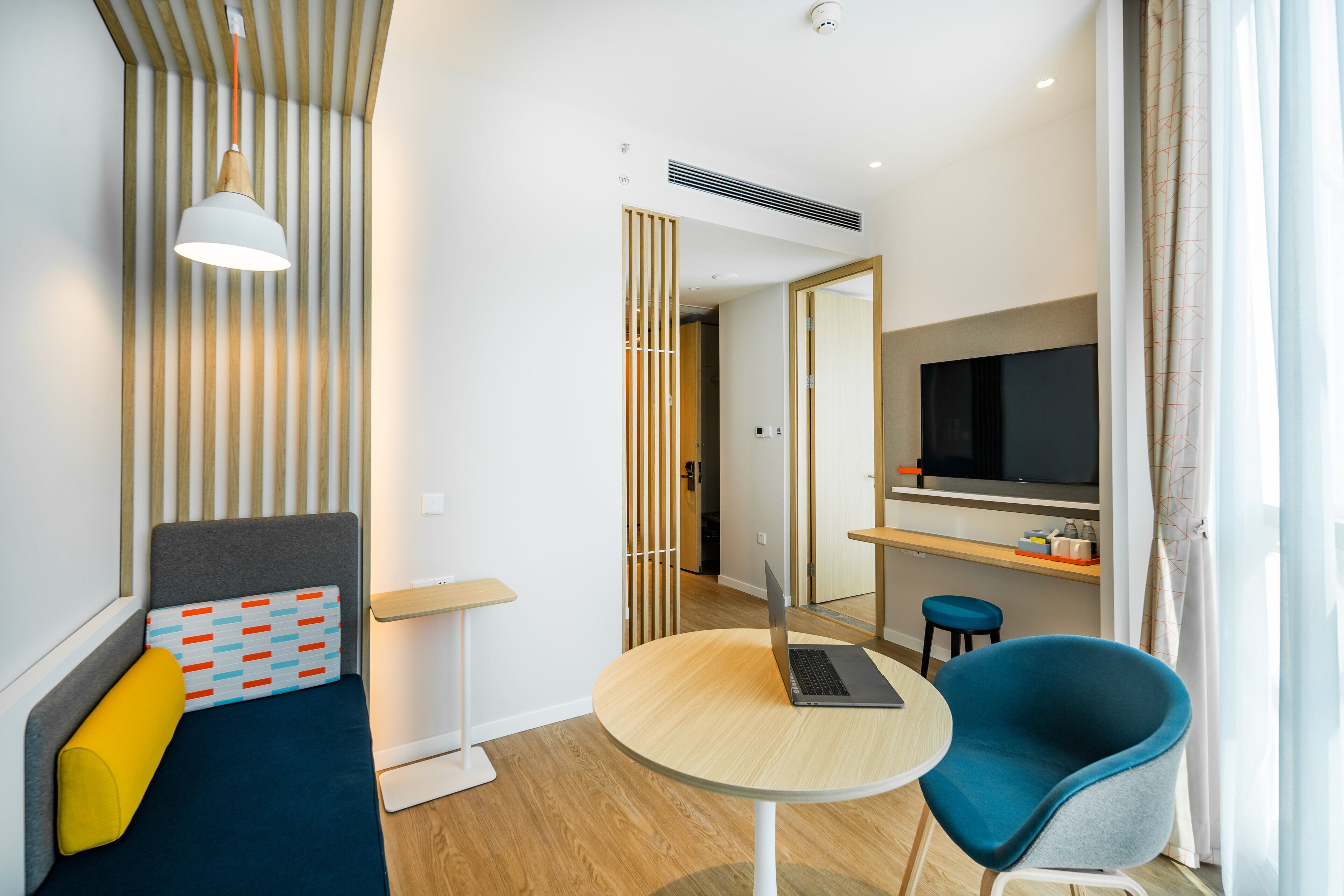 Een moderne hotelkamer met een bed, een bureau met een laptop, een televisie en een stoel.