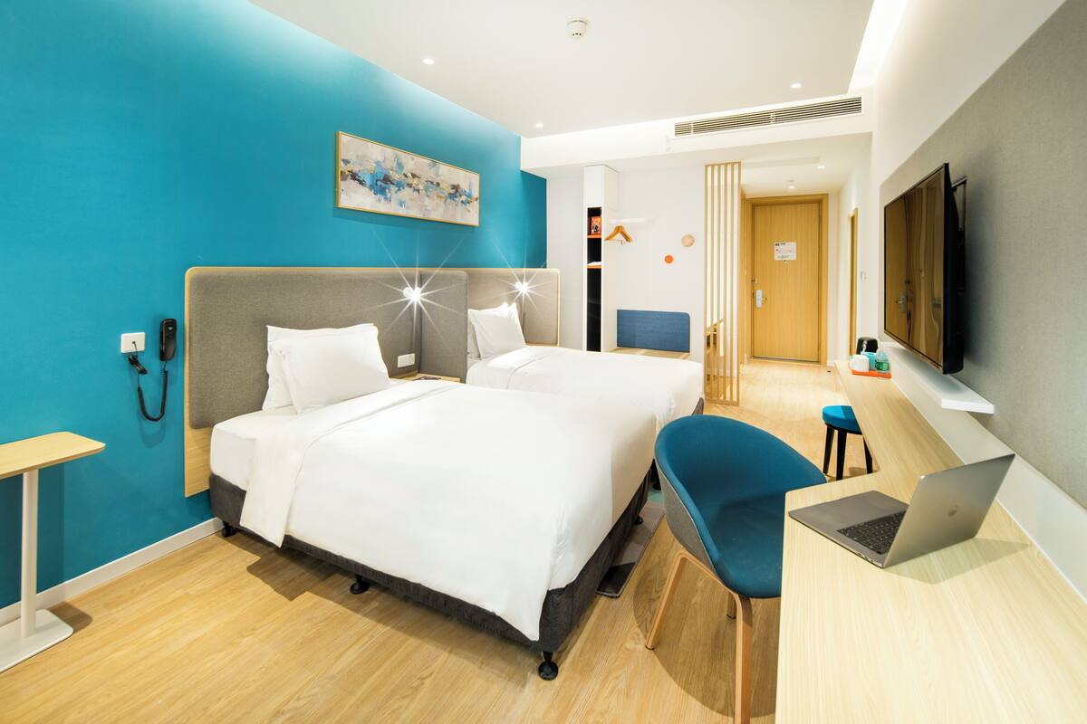 A modern hotel room with a large bed, a desk with a laptop, a TV, and a blue accent wall.