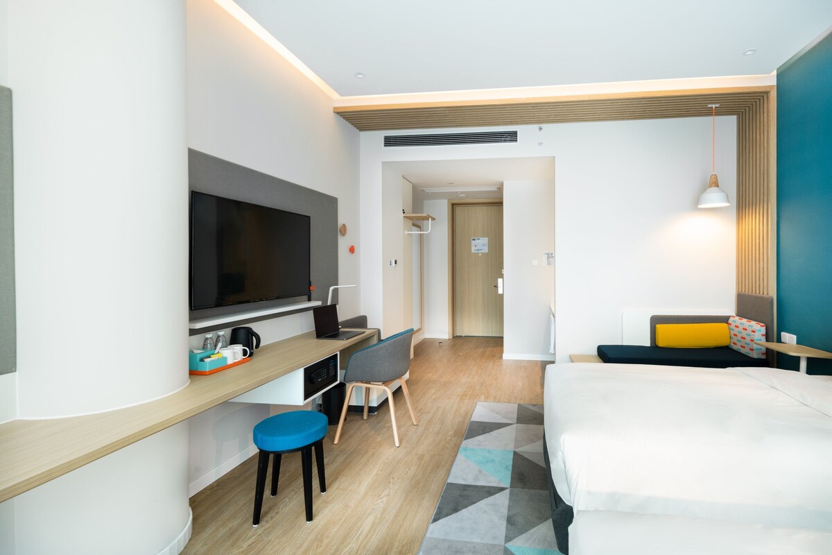A modern hotel room with a flat-screen TV, a desk with a laptop, a bed, and a seating area with a sofa and a small table.