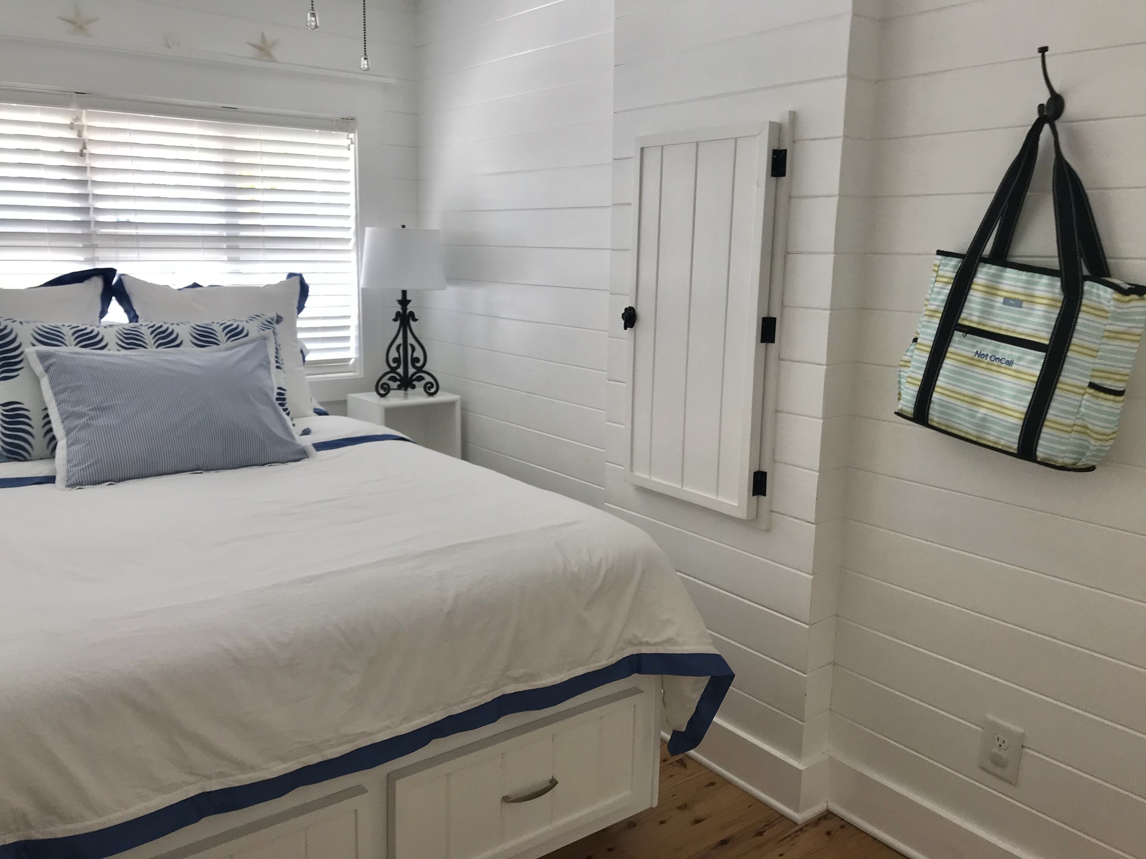 Een slaapkamer met een bed, nachtkastje, lamp en een tas aan de muur.