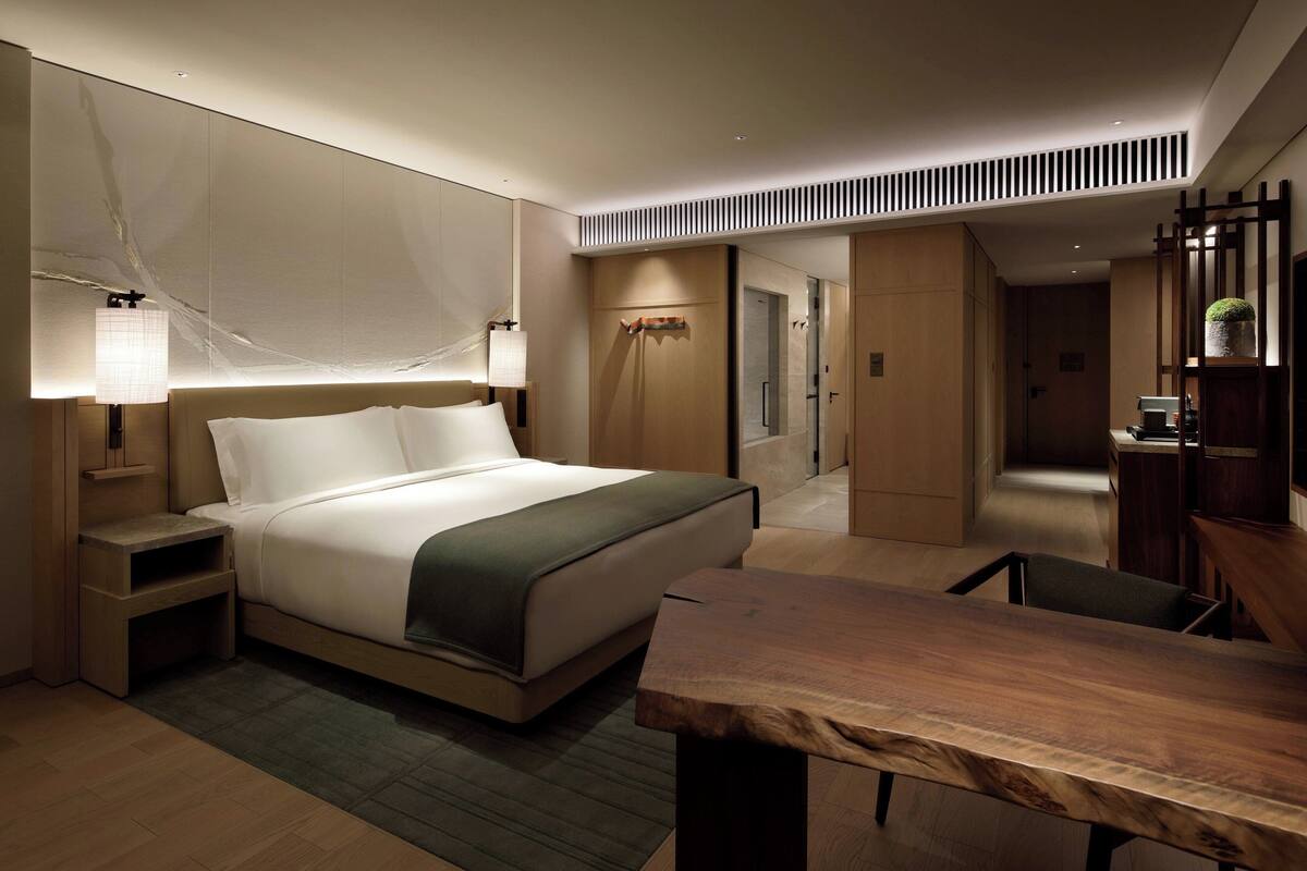A modern hotel room with a large bed, bedside tables, a wooden desk, and a mirror.
