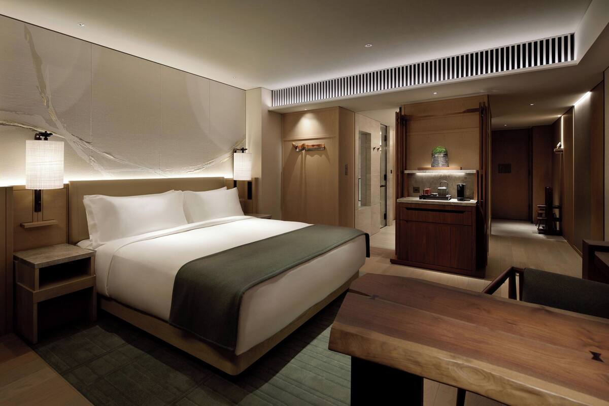 A modern hotel room with a large bed, bedside tables, a desk, and a seating area.