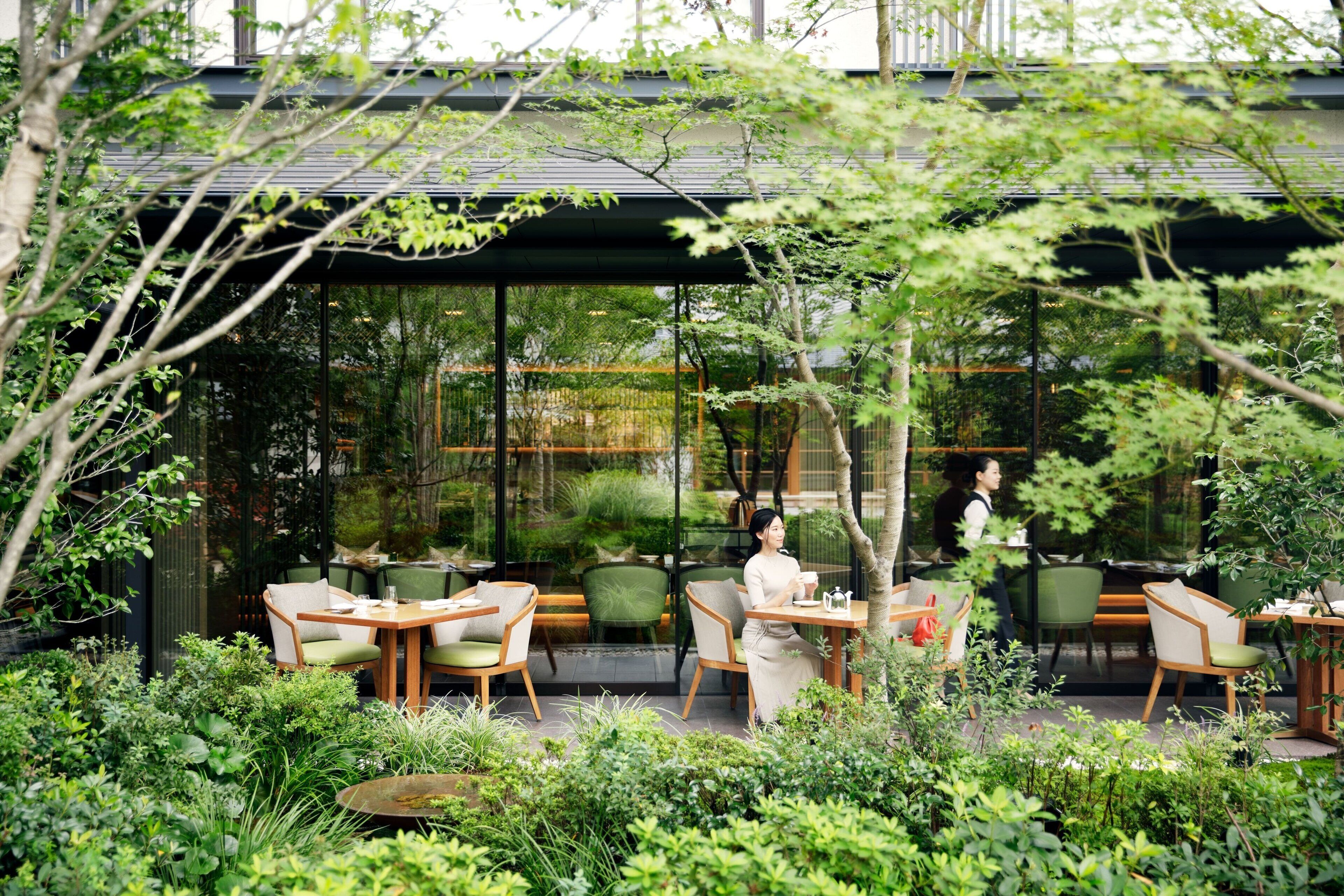 An outdoor cafe with tables and chairs, surrounded by lush greenery.