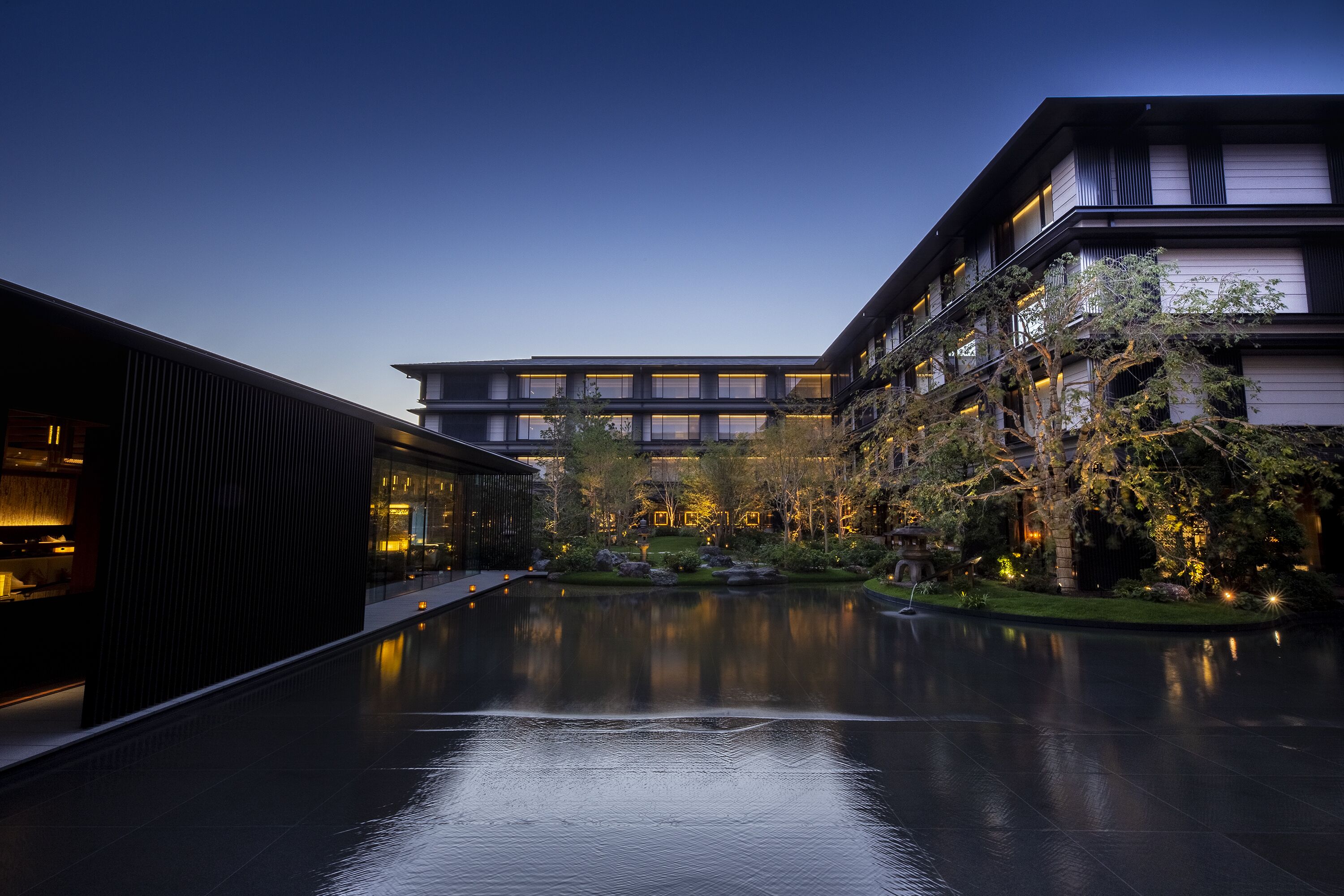 A modern building with a reflective pool in front, surrounded by trees and illuminated by ambient lighting.