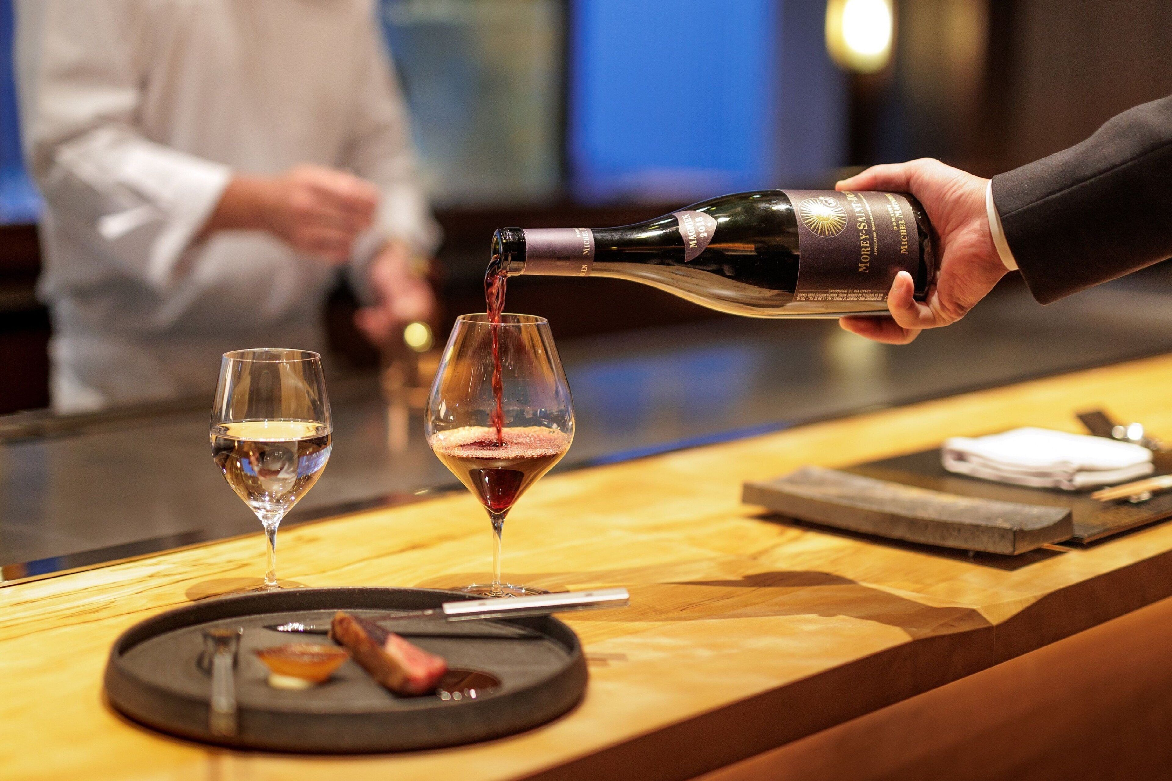 A person pouring wine into a glass at a bar.