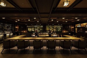A bar area with a long wooden counter, multiple bar stools, and a bartender.