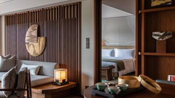 A modern hotel room with a sofa, a bedside table with a lamp, a wooden shelf with decorative items, and a bed with a green blanket.