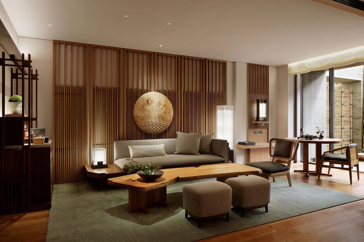 A modern living room with a sofa, coffee table, and chairs. There is a wooden partition with vertical slats and a large decorative bowl on the wall.