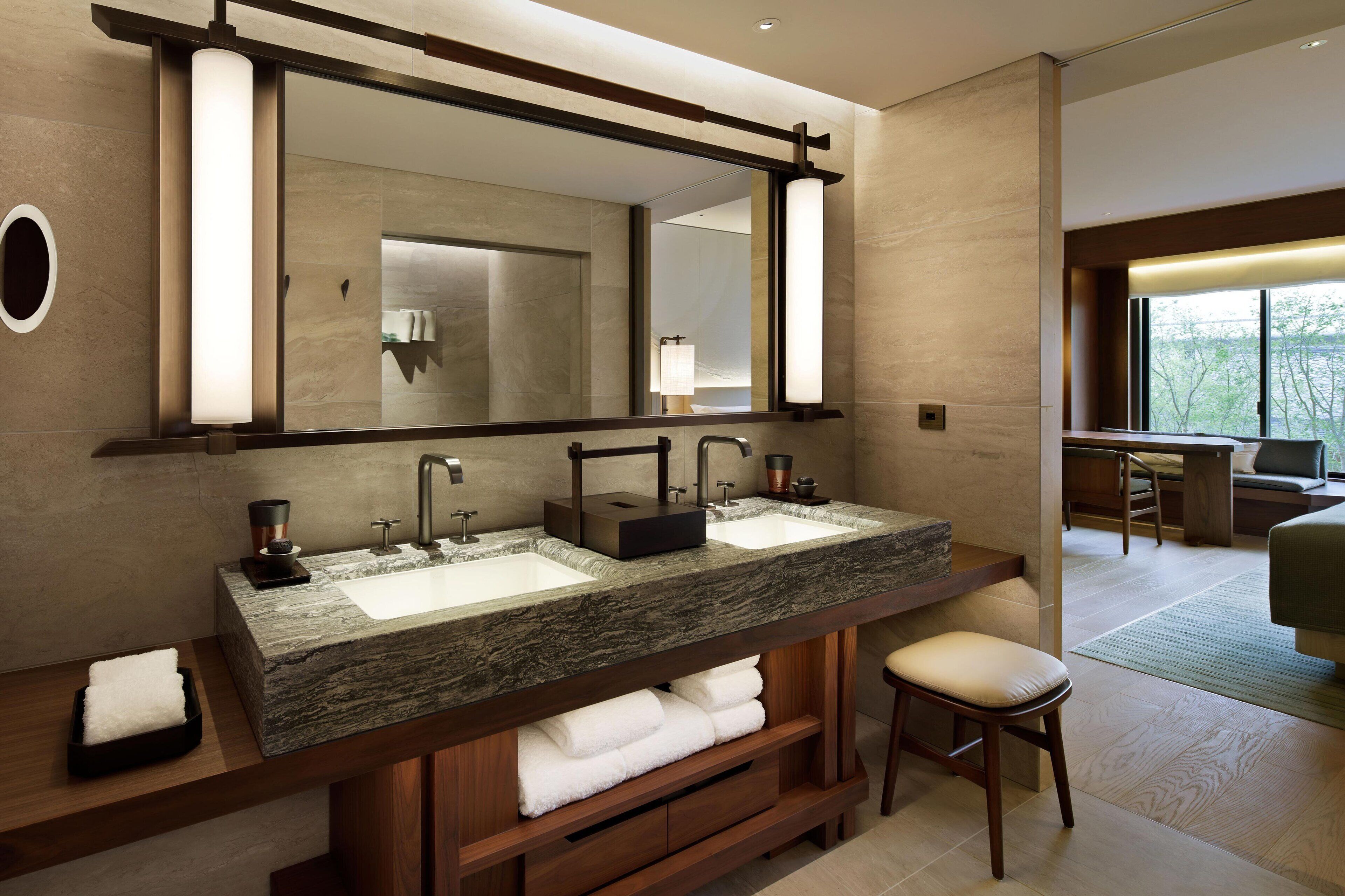 Un baño moderno con dos lavamanos, un espejo grande y una zona de estar con una silla.