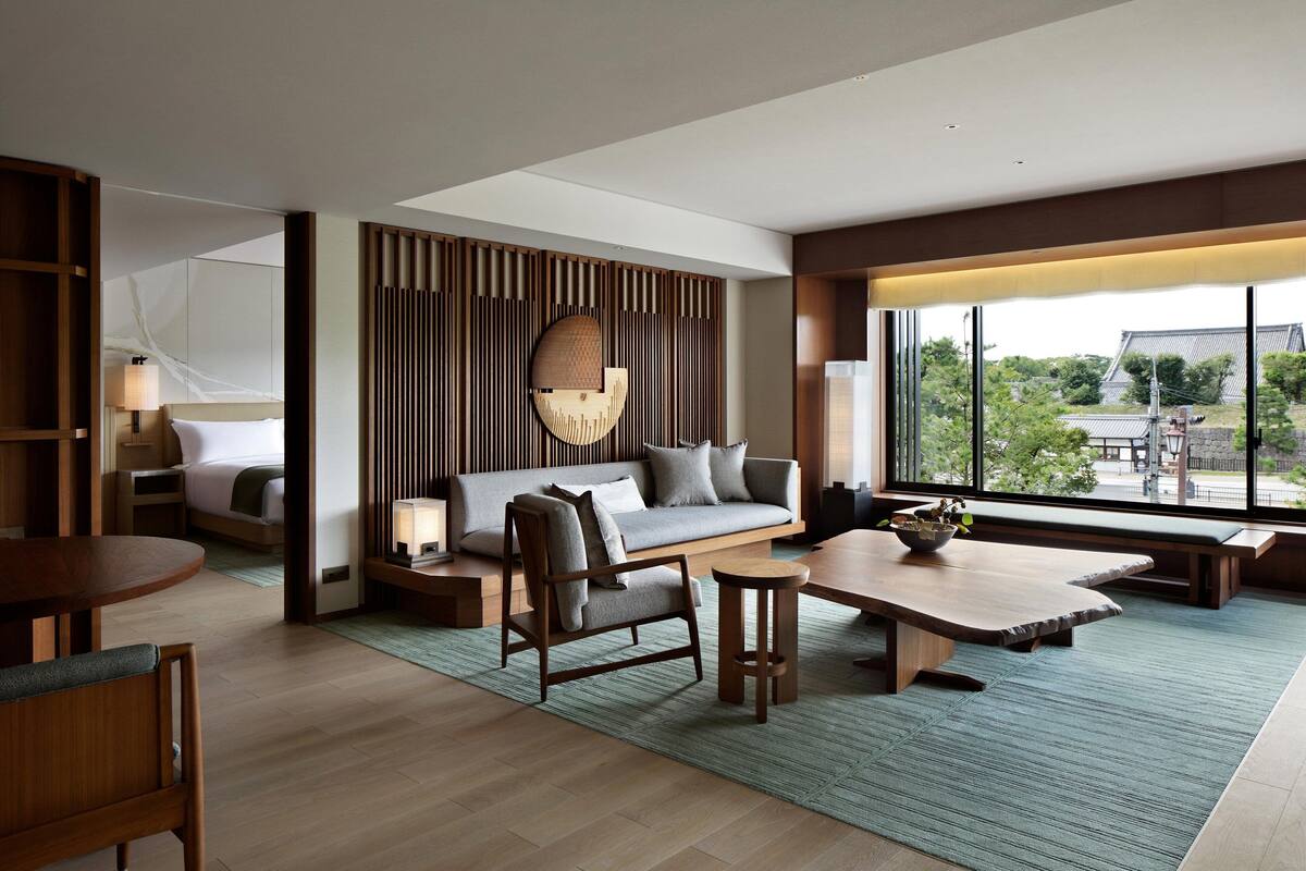 A modern hotel room with a sofa, a dining table, a chair, and a view of the outside.