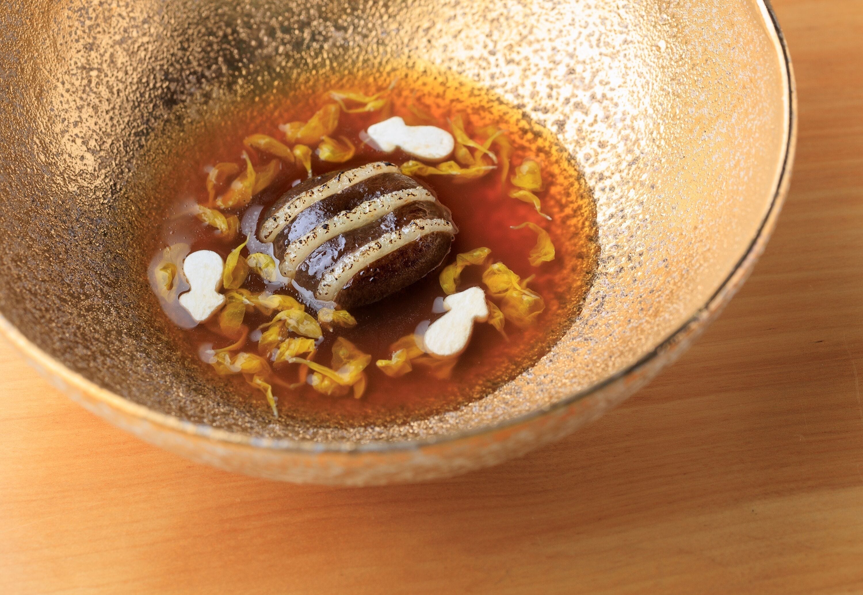 A bowl containing a food item with a liquid, possibly a soup or sauce, and some garnishes.