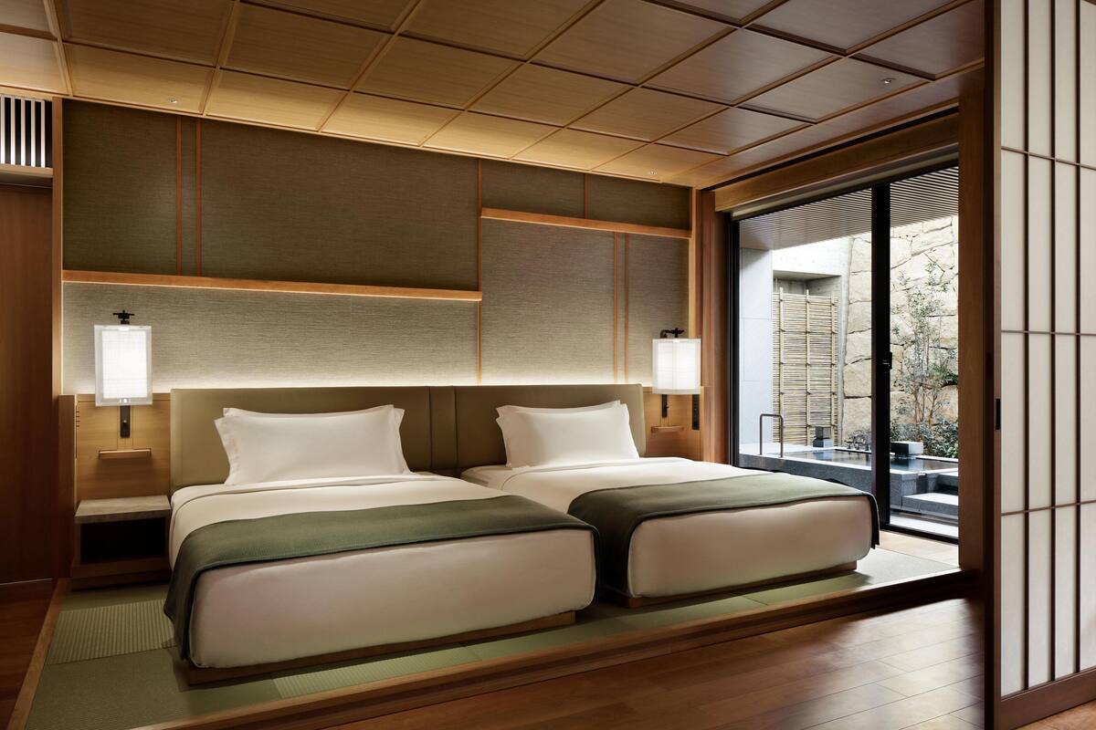 A hotel room with two beds, a large window, and a traditional Japanese sliding door.