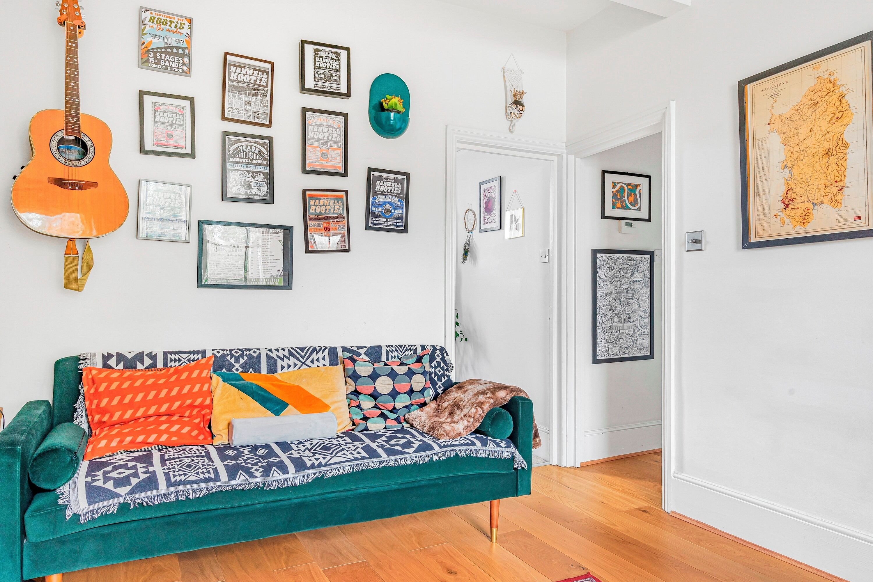 A room with a teal sofa, a guitar, and various framed posters on the wall.