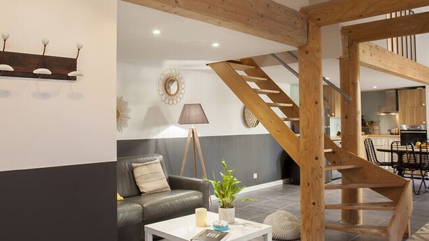 Ett rymligt vardagsrum med modern design, inrett med en trappa, en soffa, ett soffbord och en matplats.