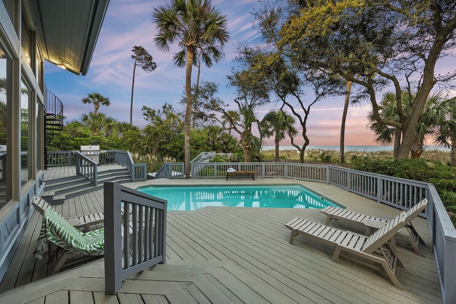 A pool with a wooden deck, surrounded by palm trees and a view of the ocean.