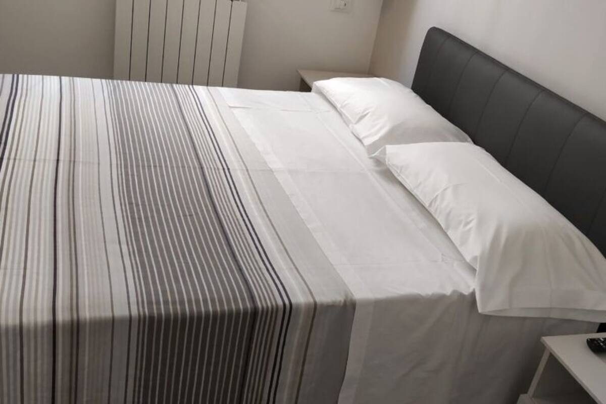 A bed with striped bedding, a black headboard, and a bedside table with a remote control.