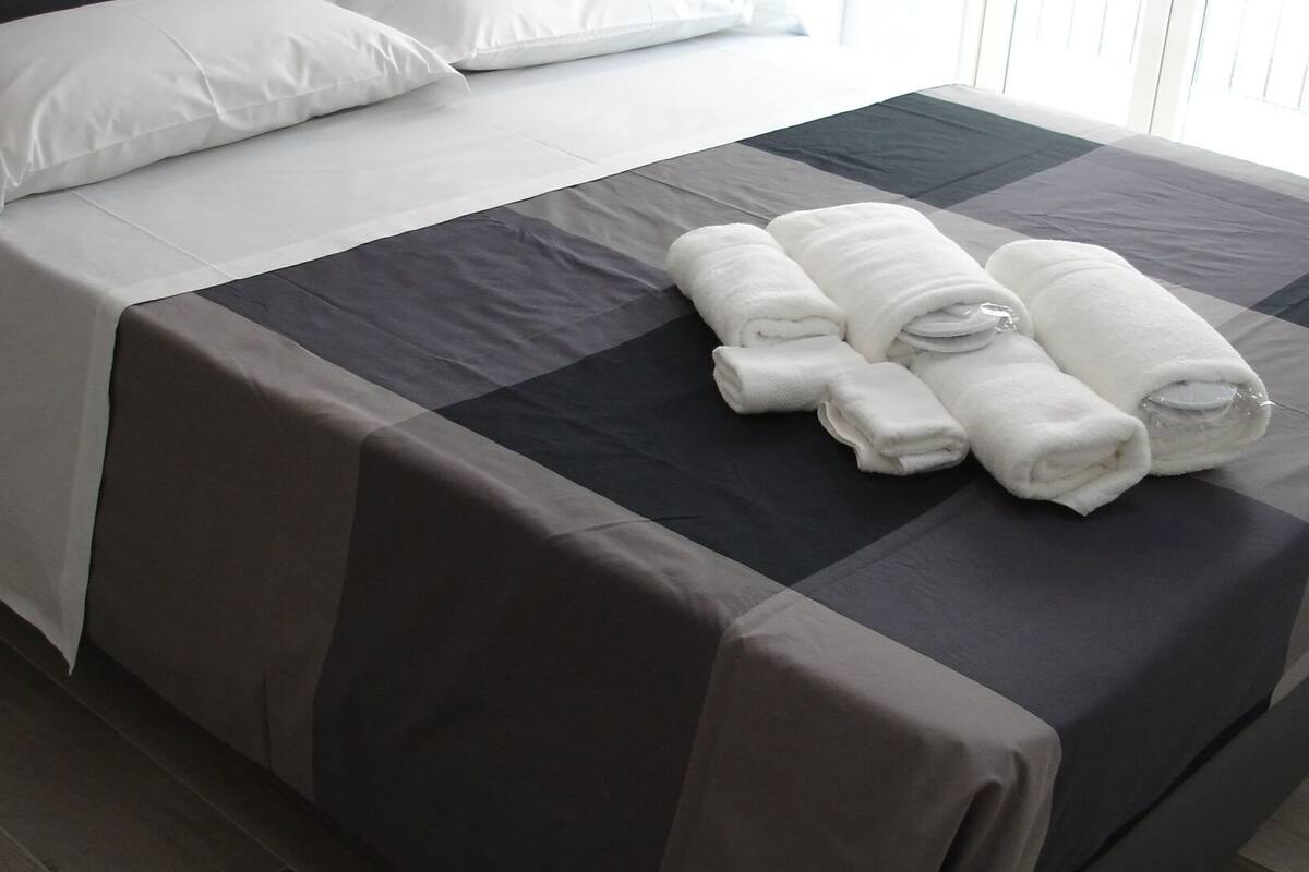 A neatly made bed with a checkered bedspread and rolled white towels.
