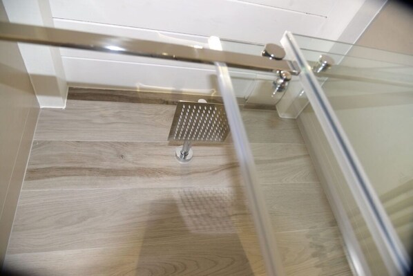 A modern shower area with a glass partition, wooden floor, and a metal showerhead.