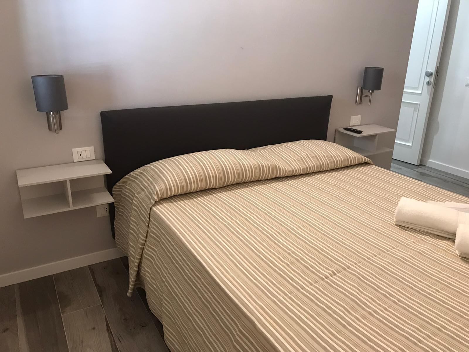Une chambre à coucher bien rangée, avec un lit, des tables de chevet et des lampes fixées au mur.