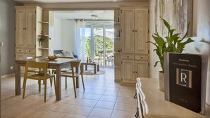 A spacious kitchen with wooden cabinets, a dining table, and chairs. There is a potted plant on the counter and a book titled "Résidence Les Laureirs Roses". - Mare, appart avec jardin et bbq, vue mer et montagne, plage et port à 2 pas (Calvi)
