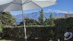 A patio area with a white umbrella, a metal pole, and a view of mountains and a lake. - Mare, appart avec jardin et bbq, vue mer et montagne, plage et port à 2 pas (Calvi)