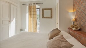 Une chambre à coucher avec un lit, une table de chevet, une lampe, une fenêtre avec des rideaux et une porte.