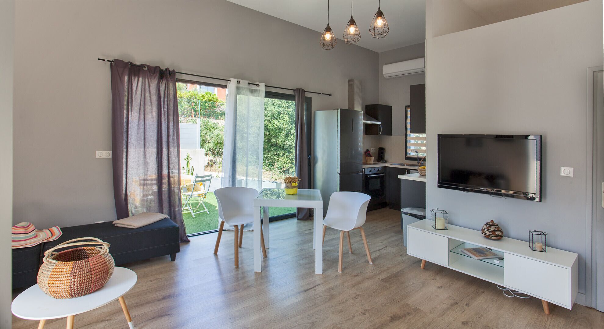 A modern living room with a sofa, chairs, a dining table, a TV, and a kitchen area.