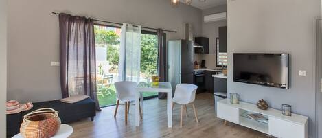 A modern living room with a sofa, chairs, a dining table, a TV, and a kitchen area.