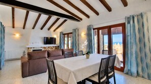 A dining area with a table and chairs, a sofa, a TV, and a view of the sea.