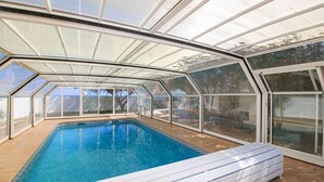 A swimming pool with a glass enclosure, surrounded by a wooden deck.