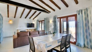 A dining area with a table set for six, a sofa, and a TV mounted on a stone wall.