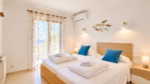 A hotel room with a double bed, two pillows, a bedside table with a lamp, and a window with curtains.