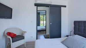 Un dormitorio con cama, una silla, un armario y un televisor en la pared.