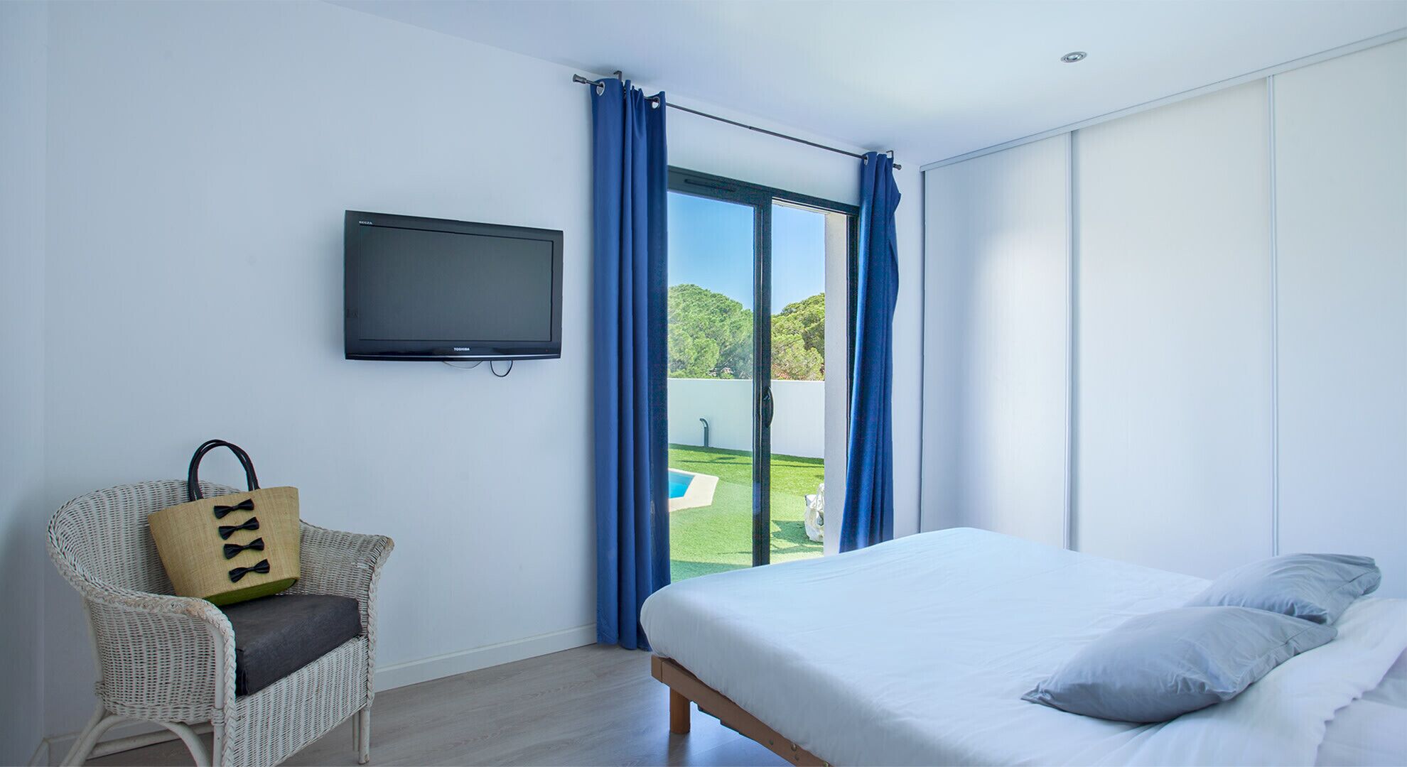 Quarto com cama, poltrona, televisão e vista para uma piscina.