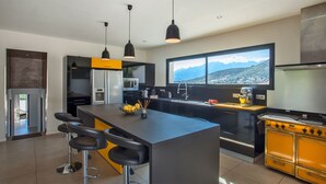 Cocina moderna con una isla central, taburetes de bar, estufa y un ventanal con vistas a la montaña.