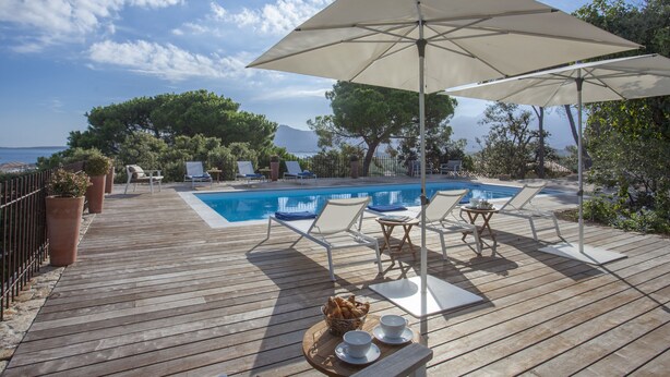 Terraza de madera con piscina, sillas de descanso y una sombrilla que da sombra.