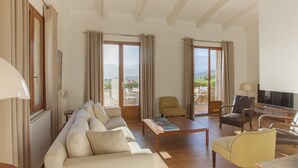 Amplia sala de estar con sofá, sillones, una mesa de centro y televisión. Cuenta con ventanas grandes con cortinas, vistas al exterior y un balcón.