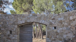 Un arco de piedra que conduce a una puerta de madera, rodeado de árboles y un muro de piedra.