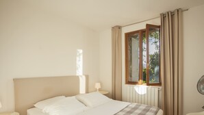 Un dormitorio con cama, mesita de noche, ventana con cortinas y radiador.