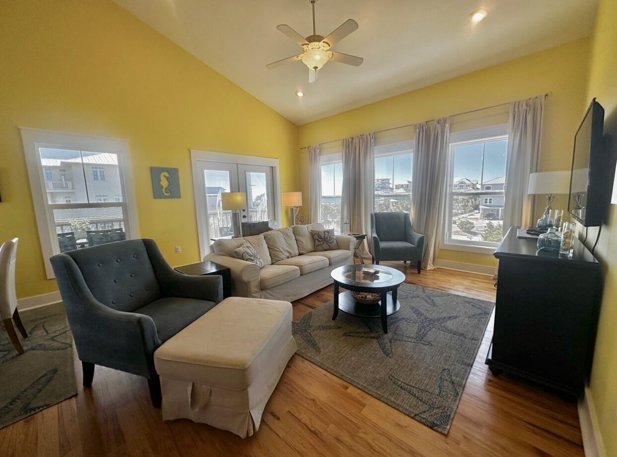 A living room with a sofa, armchair, ottoman, coffee table, and a ceiling fan.