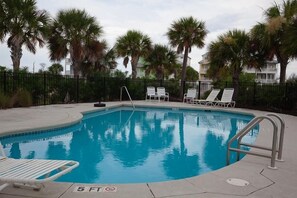 Une piscine dont la profondeur maximale est indiquée à 1,5 mètre, entourée de palmiers et de chaises longues blanches.